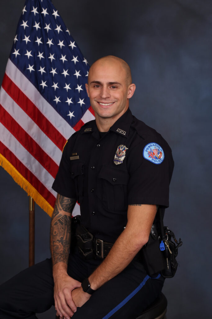 Smiling police officer in uniform sitting in front of an American flag.