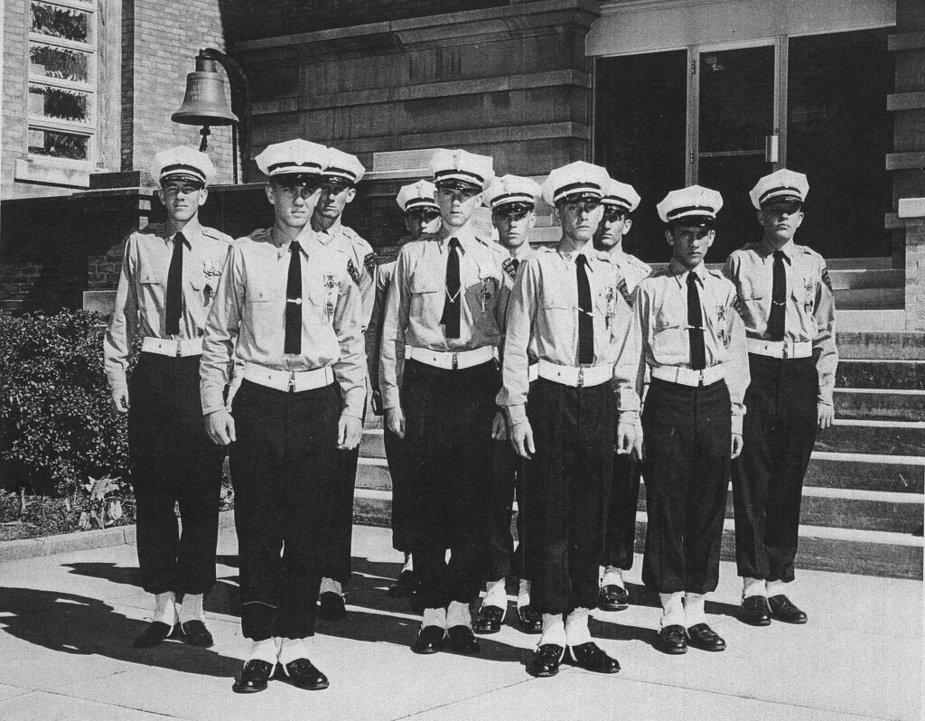 Nine members of the Pensacola Police Explorers post dressed in uniforms, standing in formation in front of a building.