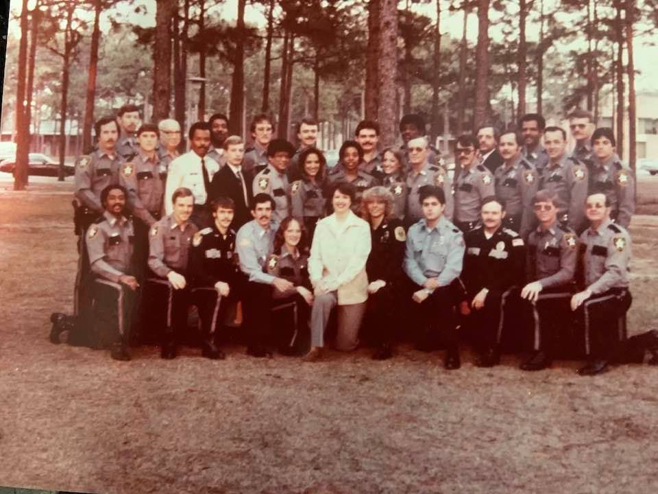 Group photo of law enforcement officers and trainees at Pensacola Junior College, taken in the past, with trees in the background.
