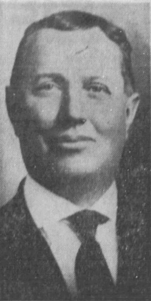 Black and white portrait of a man with short hair and a suit, presenting a serious expression.