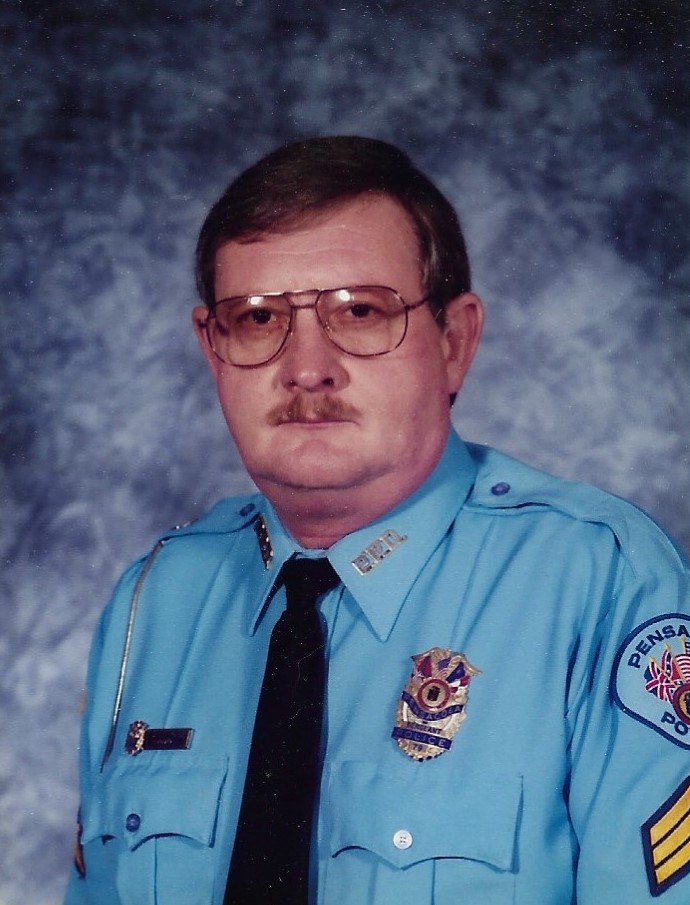 Portrait of a uniformed police officer from the Pensacola Police Department, wearing glasses and a light blue uniform shirt with badges.