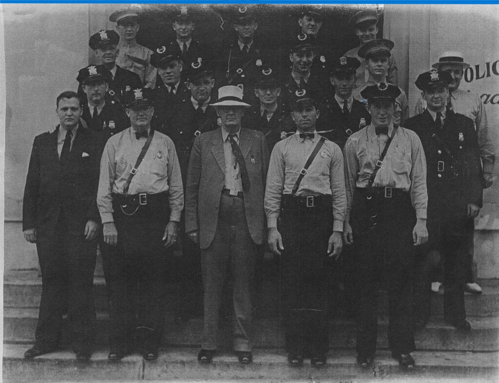 Historical photo of early law enforcement officers posing outside, featuring men in police uniforms and hats, with some wearing bow ties.