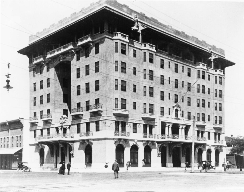 Historic black and white photograph of the San Carlos hotel in Pensacola, showcasing its architectural design and the surrounding street scene.