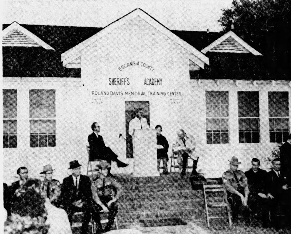 Historical photo of the Escambia County Sheriff's Academy, featuring a speaker addressing an audience seated on stairs outside the Roland Davis Memorial Training Center.