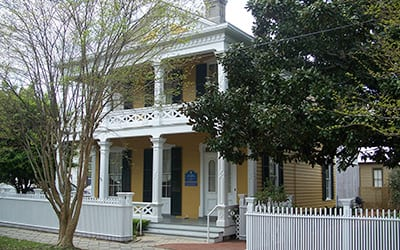The Dorr House in downtown Pensacola, a beautifully restored historic home from the late 1800s, featuring a yellow exterior and white pillars surrounded by green trees.