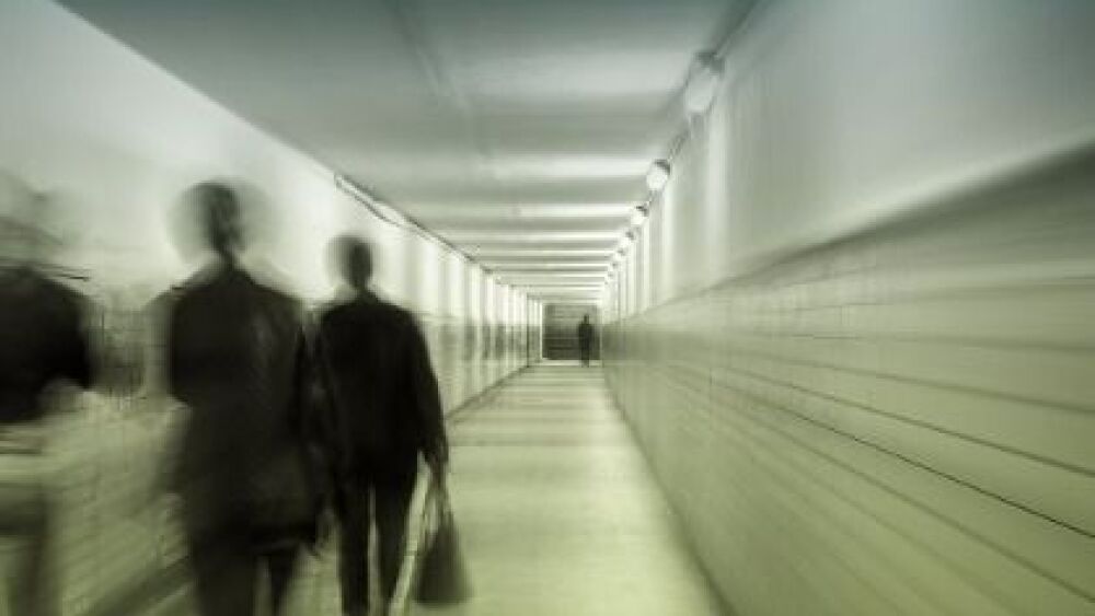 A blurred image of a long, narrow hallway with figures walking and a solitary person standing in the distance.