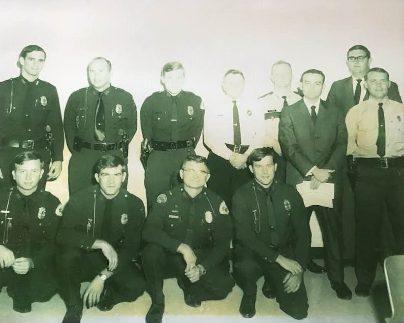 A group of police officers and officials posing for a photograph, featuring individuals in uniform and formal attire, captured in a vintage style.
