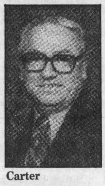 Black and white image of a man with glasses and a patterned tie, smiling for a portrait photo.