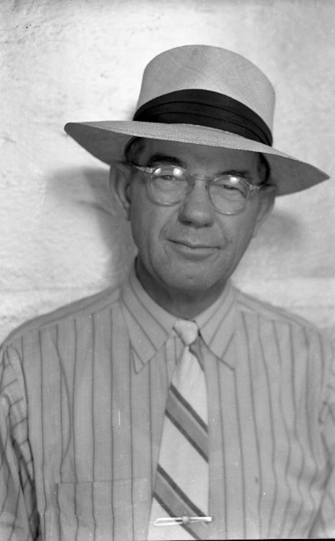 A man wearing a wide-brimmed hat and glasses, dressed in a striped shirt and tie, posing for a portrait.