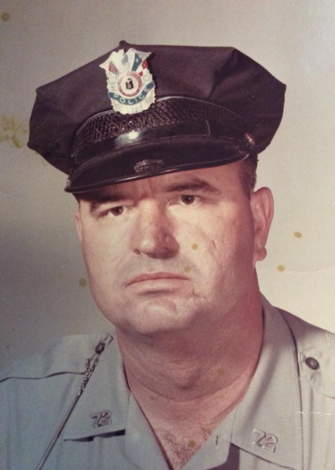 Close-up portrait of a police officer in uniform, wearing a police cap with insignia, looking serious.