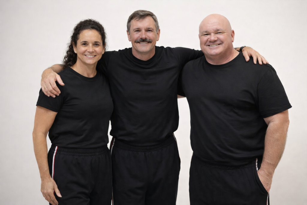 Three people dressed in black athletic wear posing together with smiles in a neutral background.