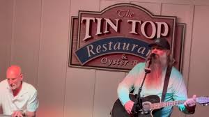 Two musicians performing on stage at The Tin Top Restaurant and Oyster Bar, with one playing guitar and the other on keyboards.