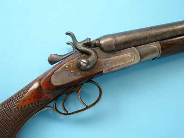 Close-up view of a vintage shotgun resting on a blue background, showcasing its wooden stock and metal mechanisms.