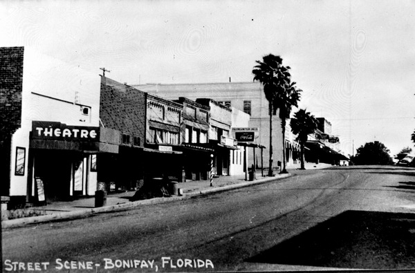 Black and white image of a street scene in Bonifay, Florida, featuring storefronts, including a theater, and palm trees lining the road.