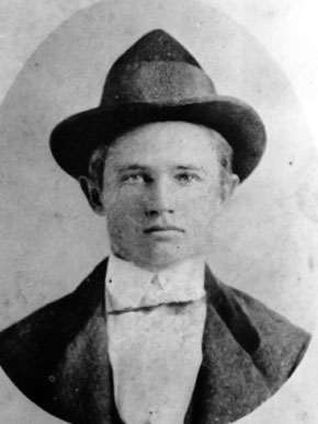 Black and white portrait of a young man wearing a hat and formal attire, looking directly at the camera.