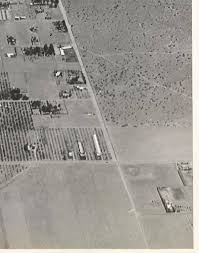 Aerial view of farmland featuring plots of crops and residential buildings, with a mix of green vegetation and barren land in a desert-like landscape.