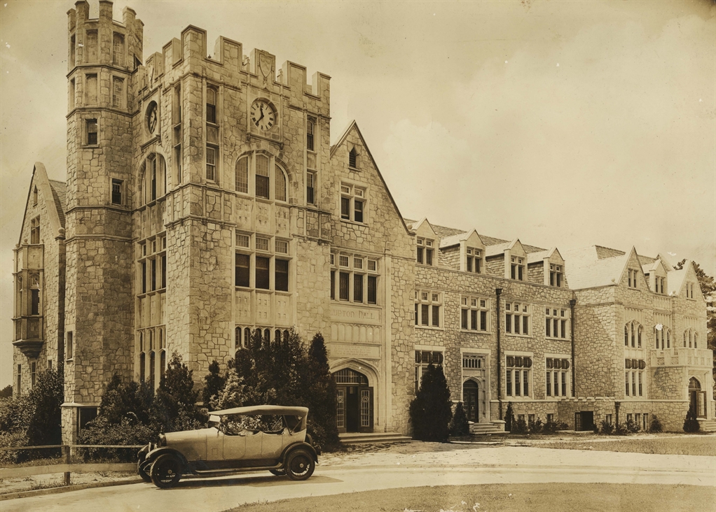 An old historical building featuring a castle-like architecture with a clock tower, accompanied by a vintage car parked in front.