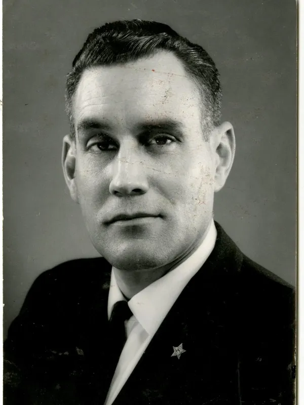 Black and white portrait of a man in a suit with a star emblem on the lapel, looking directly at the camera.