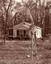 A vintage farmhouse surrounded by trees, with a windmill in the foreground.
